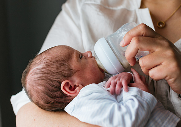 A newborn baby takes a bottle from mom